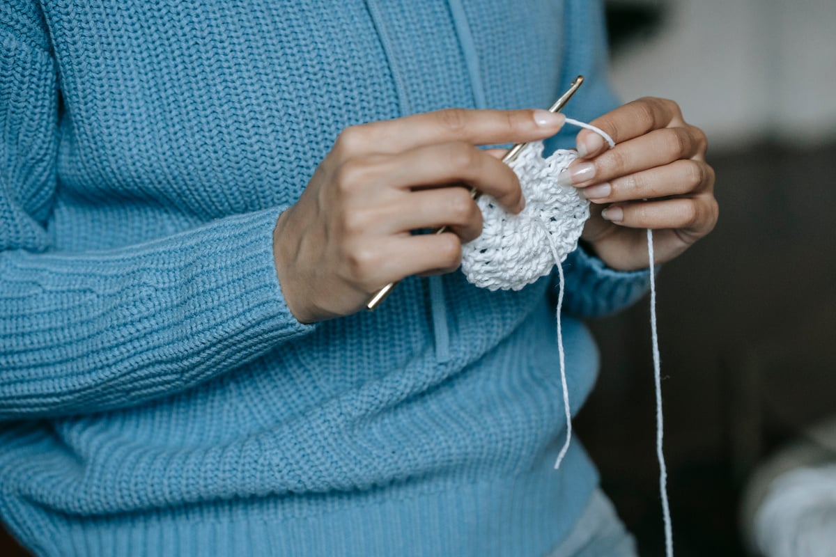 A Person in Knitted Sweater Holding a White Yarn and Crochet Hook